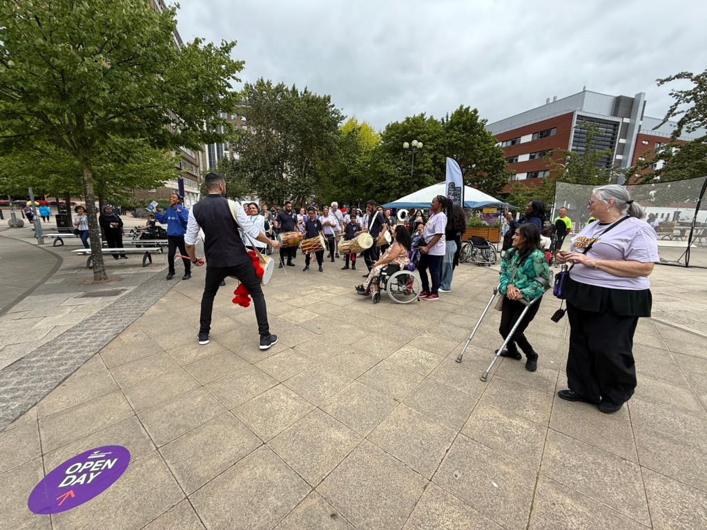 Crowd standing and sitting watching the dhol players perform at the Birmingham Disability Festival.