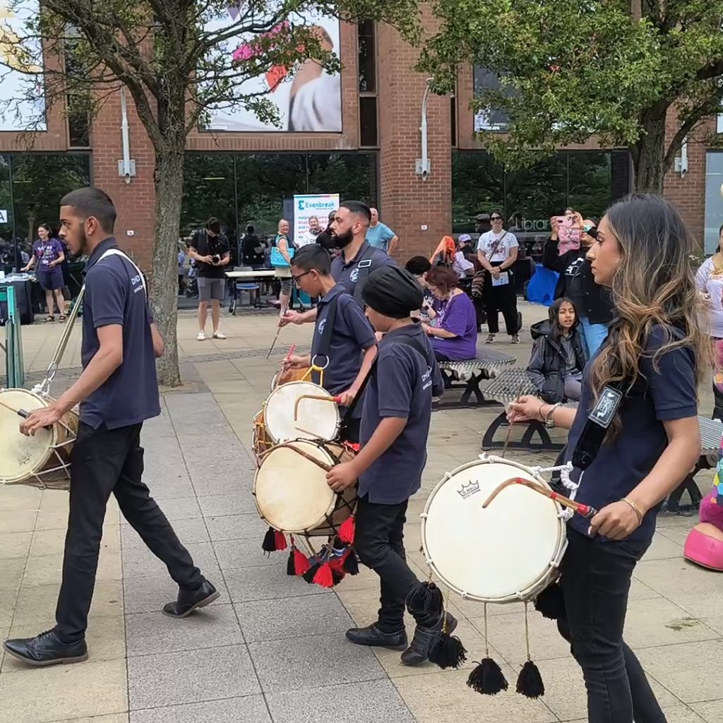 The crowd is following the dhol players procession as they walk around the university campus playing the Dhol (Bhangra drums).