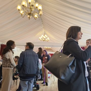 Room inside the House of Lords where the event was held. Attendees are gathered networking over lunch. The room has light fixtures on the right and left side above with a big white drape covering the ceiling.