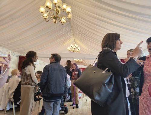 Room inside the House of Lords where the event was held. Attendees are gathered networking over lunch. The room has light fixtures on the right and left side above with a big white drape covering the ceiling.