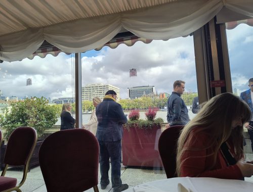 A few attendees are standing outside the room on the terrace with a view of the River Thames.