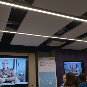 Theo Paphitis welcomes SBS attendees to the event via a video message display on TV screens on the right and left with a Small Business Sunday banner in the centre.