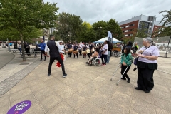Small crowd standing and sitting watching the dhol players perform at the Birmingham Disability Festival