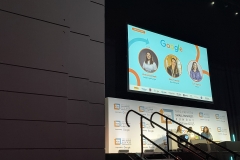 Panel discussion on stage Behind them is a screen that shows the google logo with images of the three-panel members and their names and their titles. Below the TV screen is the SBS banner that says Theo Paphitis Small Business Sunday supported by Google with their logo on a white background.